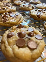 gourmet chocolate chip cookies spread out on a gold cooling rack